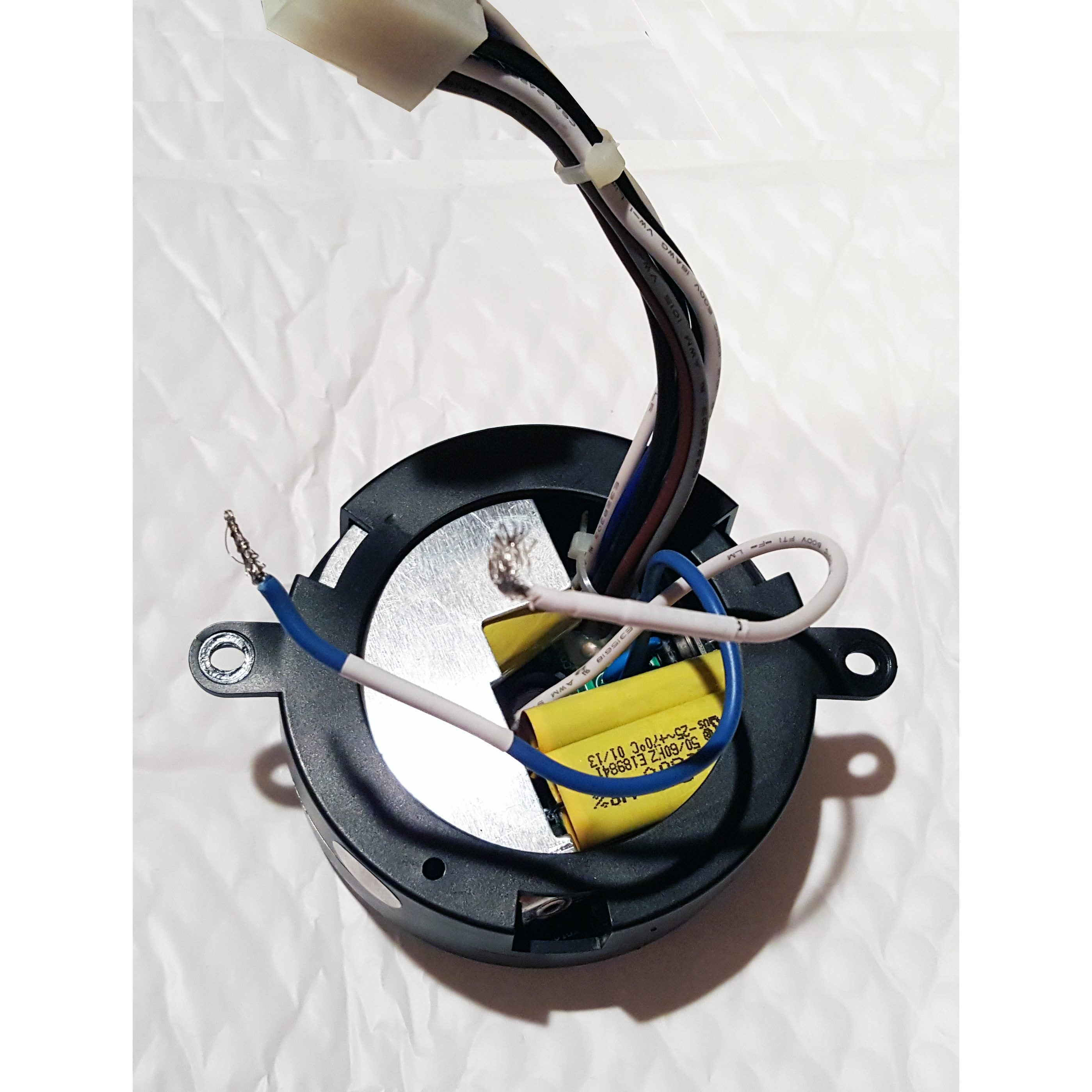 A Home Decorators Collection MR77A Ceiling Fan Remote Control Kit, a round black component with exposed wires and yellow capacitors, is placed on a white textured surface.